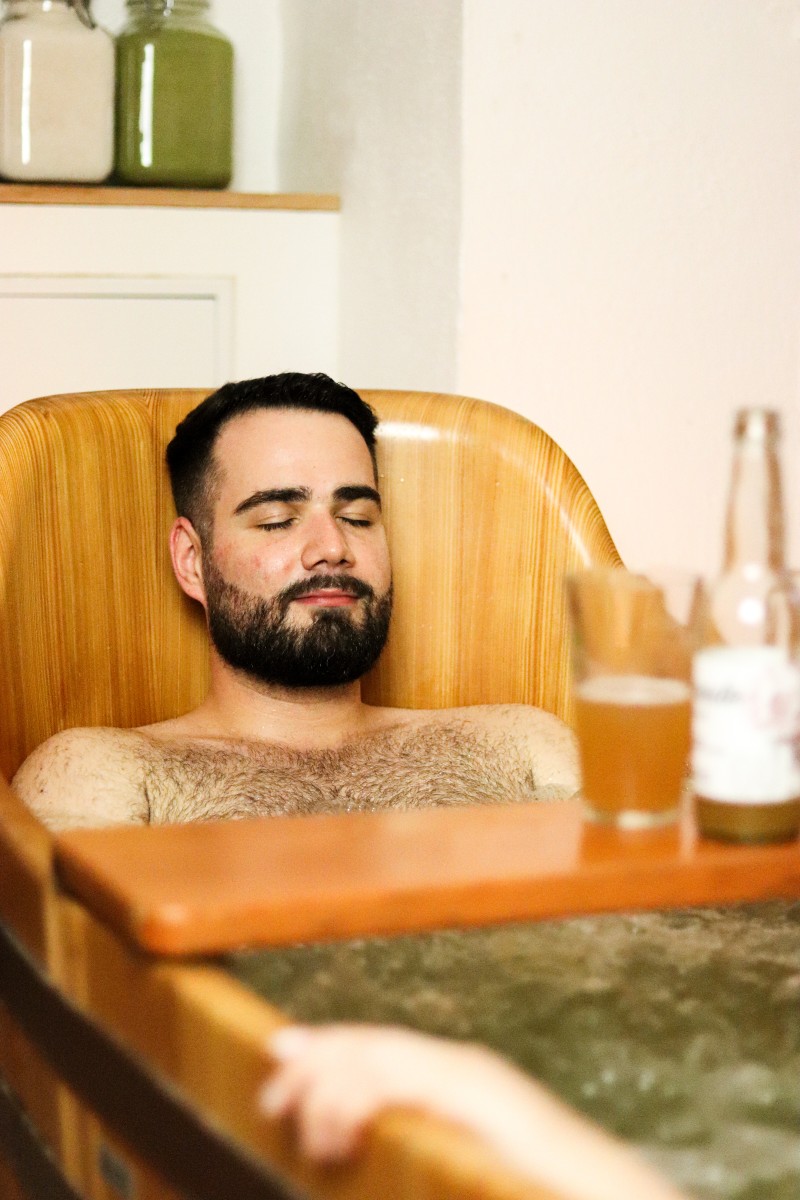 Image d'un bain de bière avec une femme dedans et une bière posée sur une planche centrale
